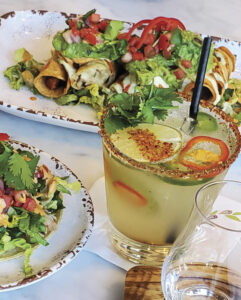 Picture of a table setting including a spicy margarita with plates of fresh greens and tacos