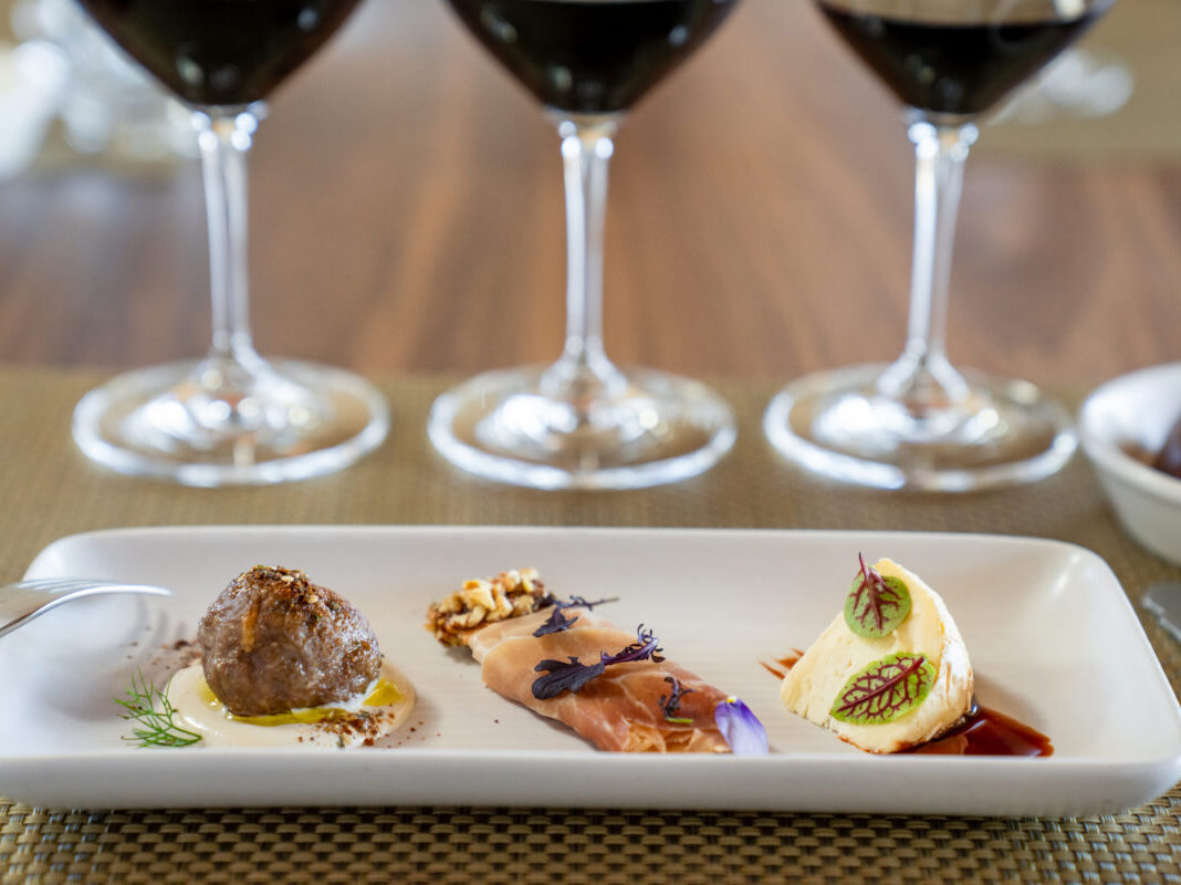 Three glasses of wine with three paired food items on a plate