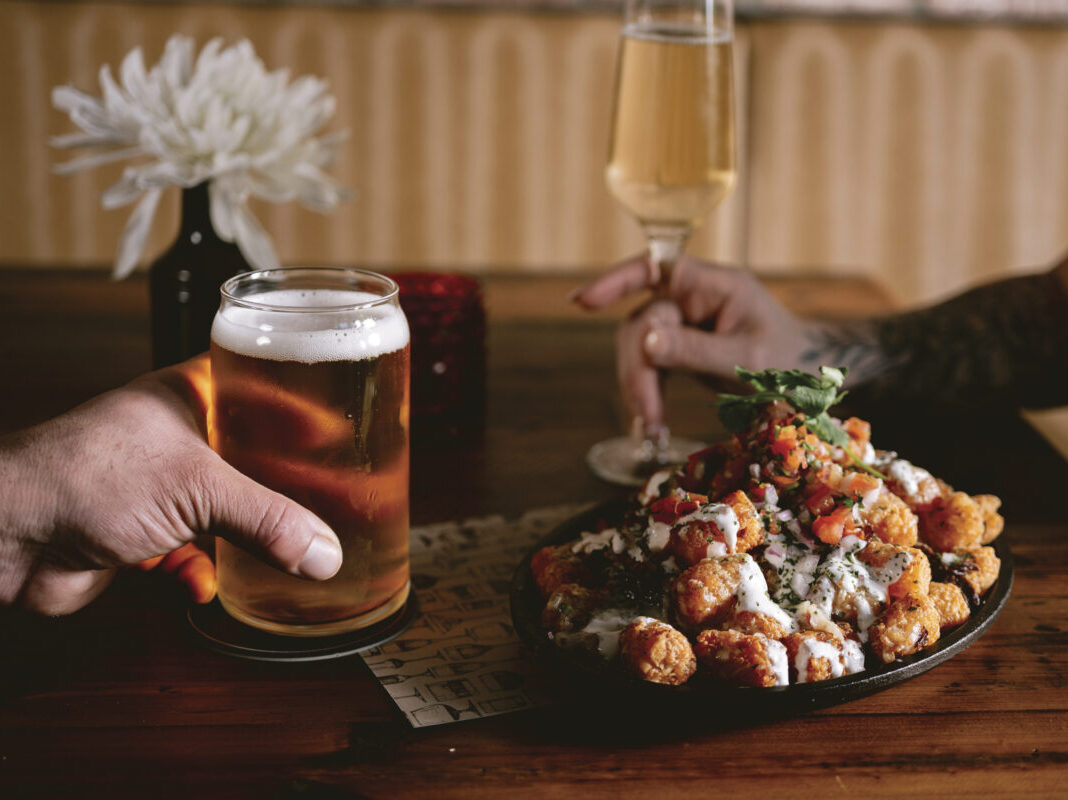 plate of food with a hand holding a beer and a hand holding a wine glass