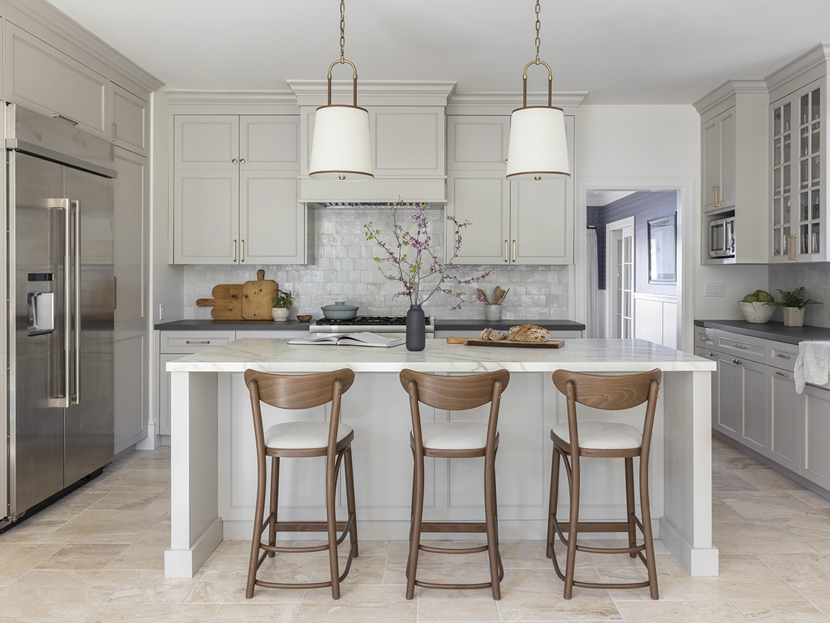 A beautiful new kitchen with taupe painted cabinets, a large stone island and bluestone countertops, with large pendants and modern barstools
