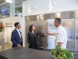 Chef opening a subzero fridge to show 2 potential clients in business suits in showroom