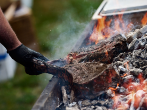 person with gloves grilling meat on an open fire