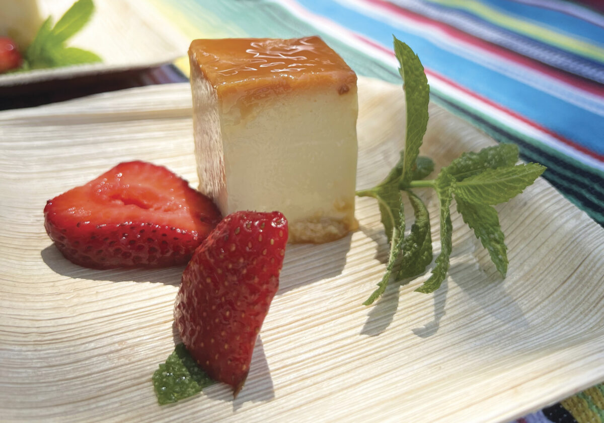 piece of flan with sliced strawberries on a bamboo plate on a striped tablecloth