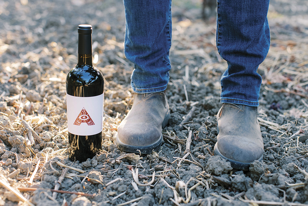 bottle of Artesa wine on ground next to person in jeans in boots