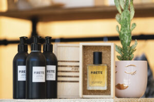 display of perfume bottle in woodem box and black bottles of accompanying body oil and plant in pot