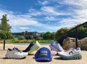 running shoes and Napa Running Company branded baseball hat on display on sidewalk with blue sky
