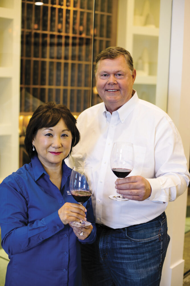Miki and Brian Cunat standing and smiling holding glasses of red wine