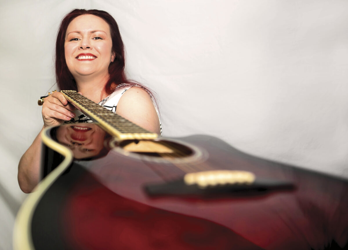 Musician Amber Snider posing with her guitar in front of a white background