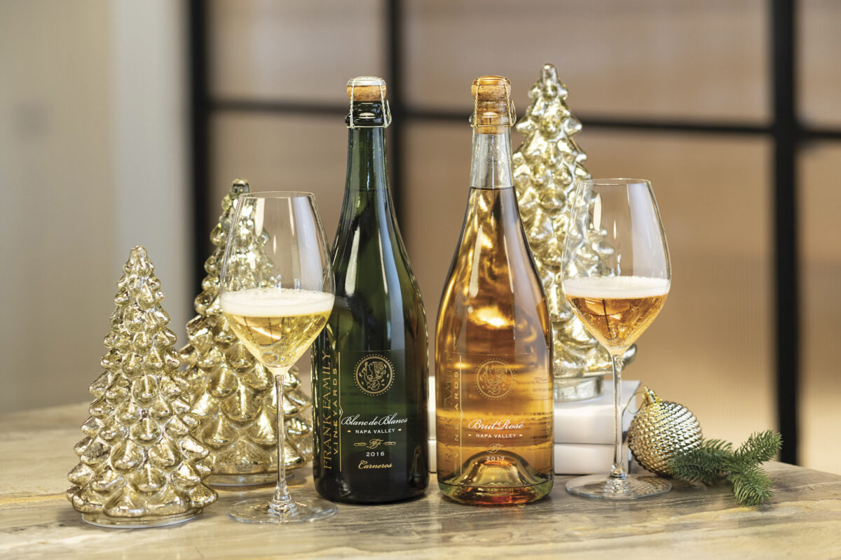 Two bottles of Frank Family Vineyards sparkling wine on a table with glass christmas tree decor and two glasses of wine