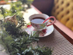 cup and saucer of tea with candy cane in it on table top with christmas tree in view