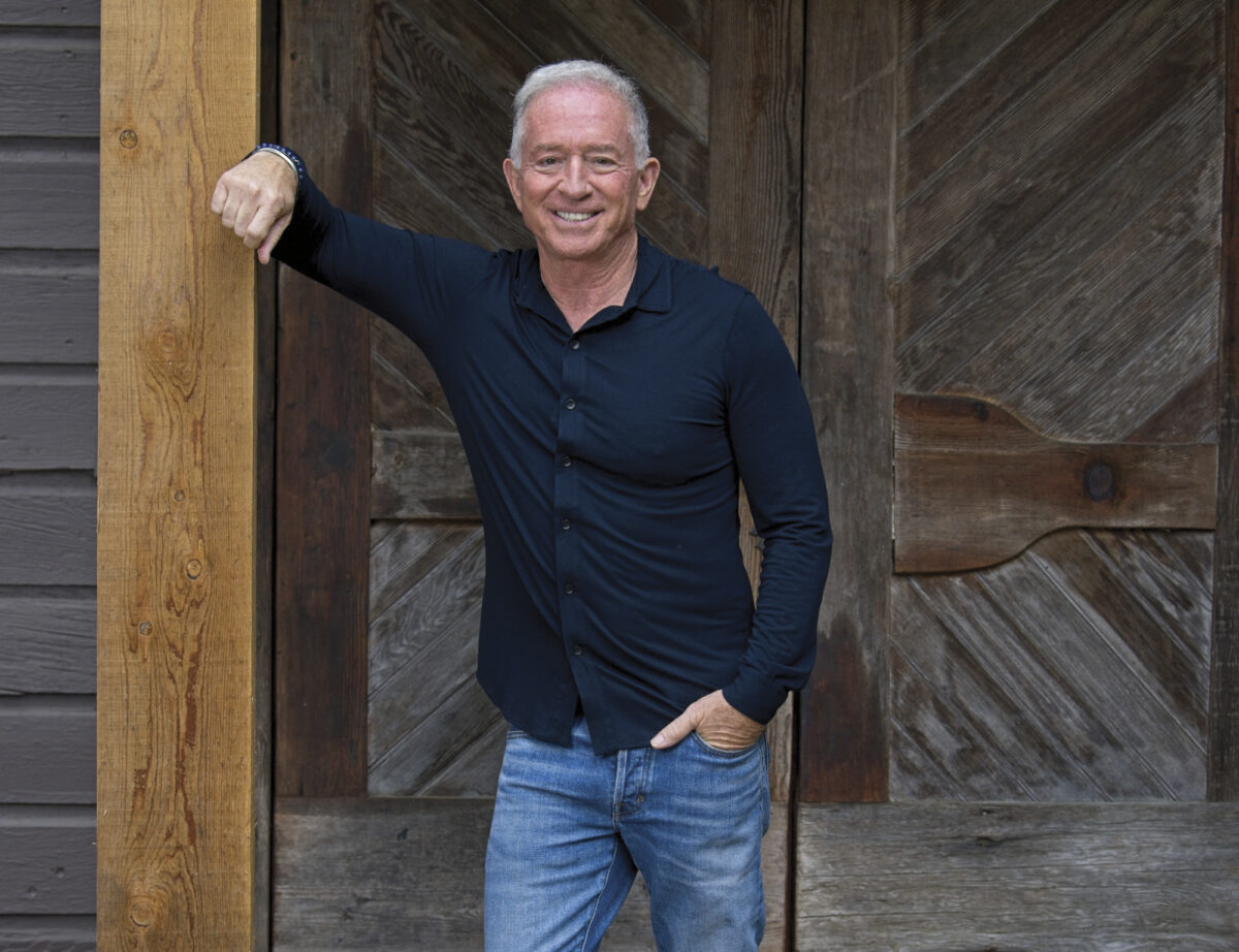 Mark Ibanez leaning on a wooden post outdoors wearing a navy shirt and jeans