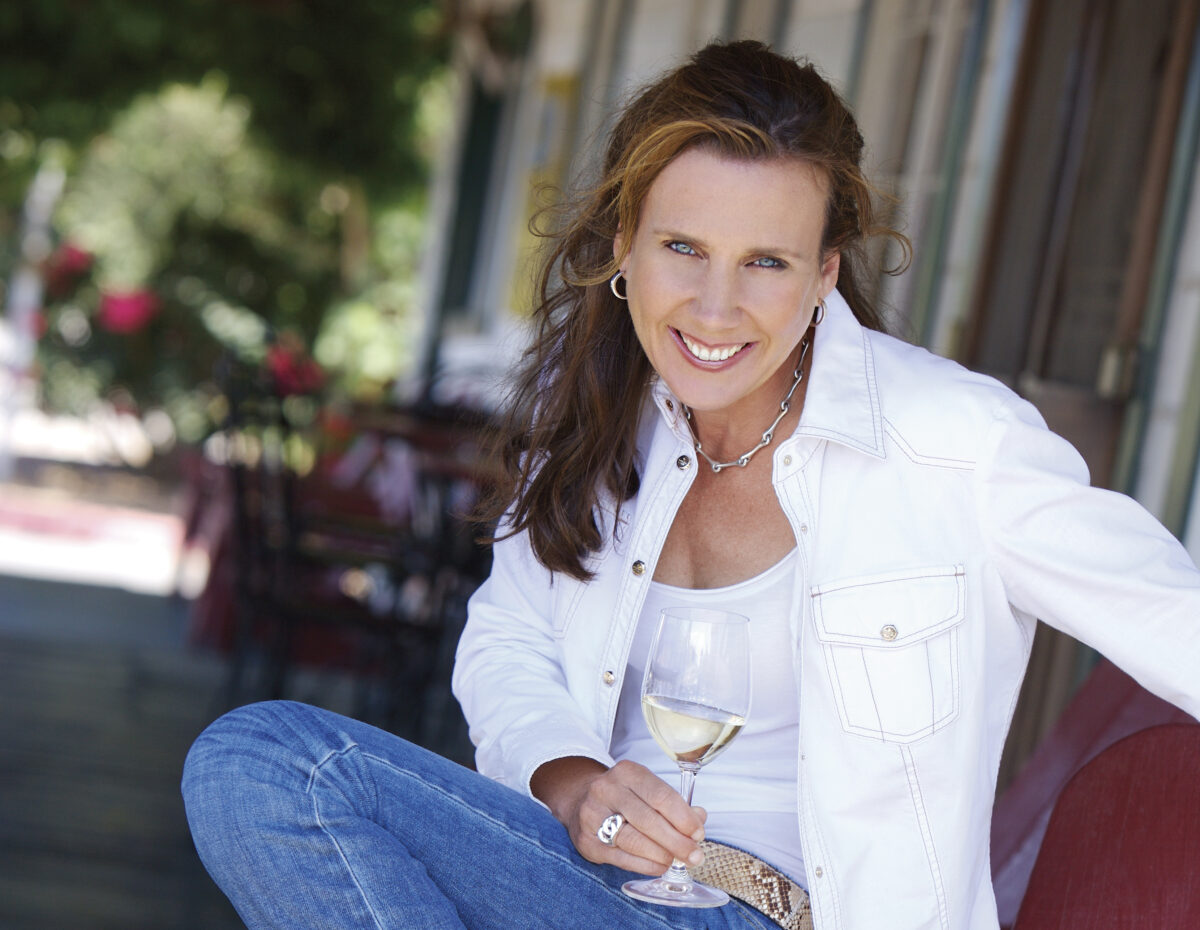 Gina Gallo on porch wearing white shirt and jeans, smiling