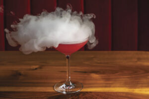 image of red cocktail in martini glass with steam coming off the top on table with red background