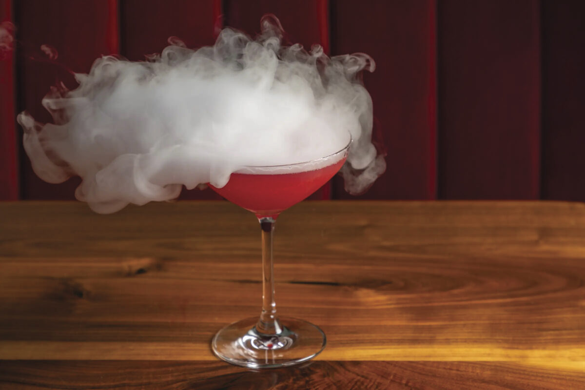 image of red cocktail in martini glass with steam coming off the top on table with red background