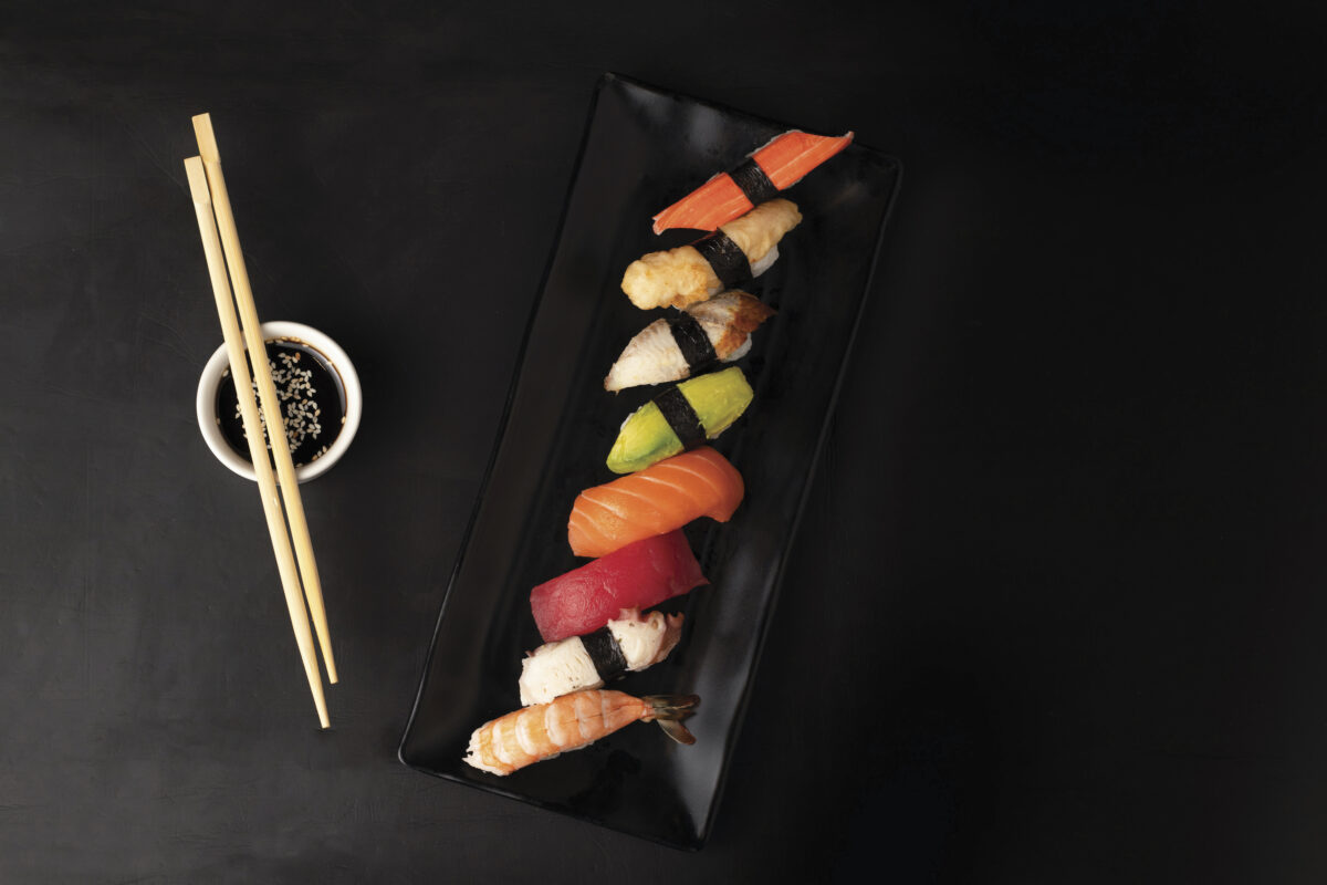 colorful plate of sushi on black table with chopsticks laying on a small white bowl of sauce