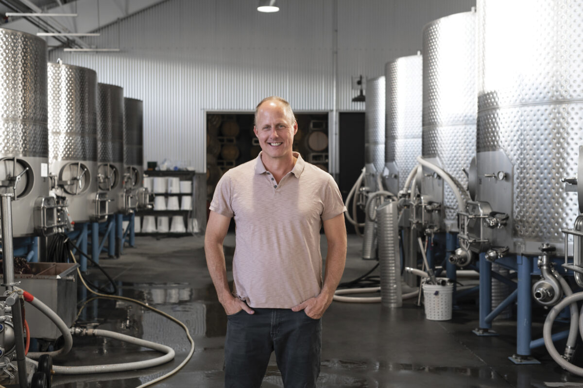 Homas Rivers Brown standing with hands in pockets in light pink polo shirt in winemaking room