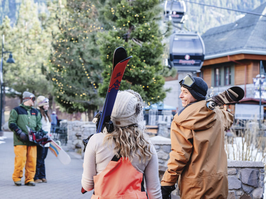 adults in winter wear walking near ski resort holding skis