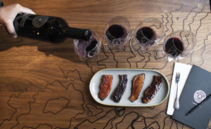 wood table top with plate with bacon and glasses of red wine