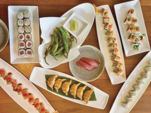 various types of colorful sushi and sushi rolls on white plates served on a wooden table