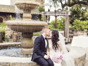 bride and groom seated on edge of outdoor fountain kissing at V. Sattui