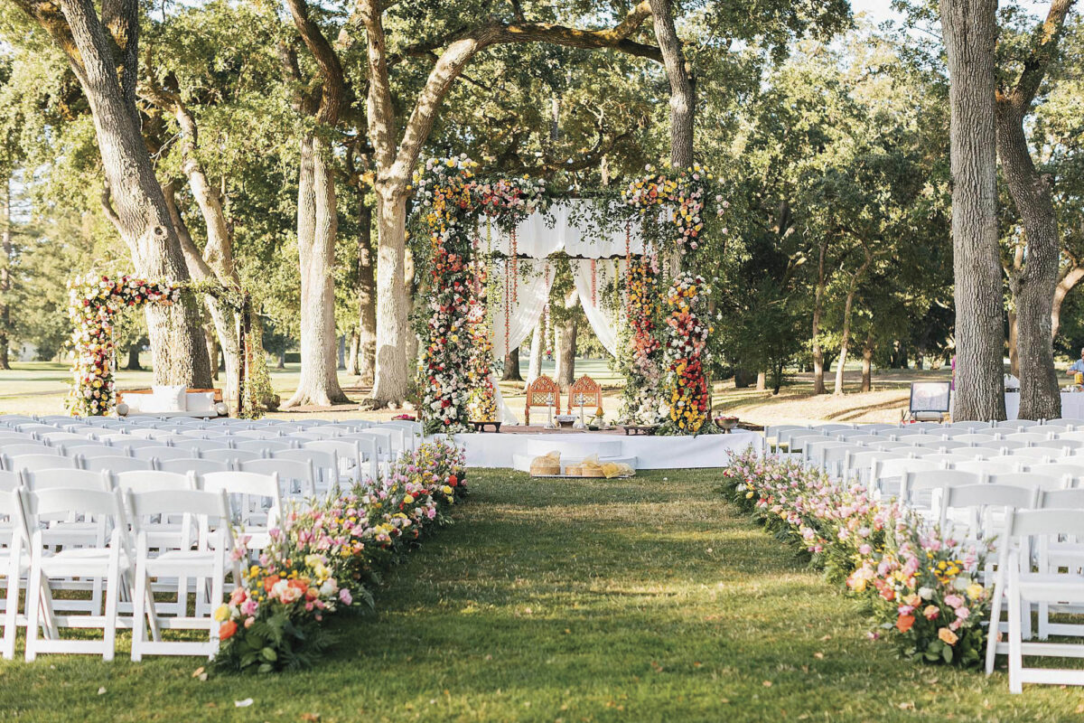 Silverado Resort grove set up for wedding ceremony on lawn with white chairs, flowers along the aisle, large trees and a canopy for the ceremony