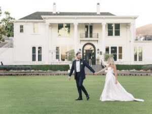 Bride and groom holding hands and walking on lawn in front of Silverado Resort, white building