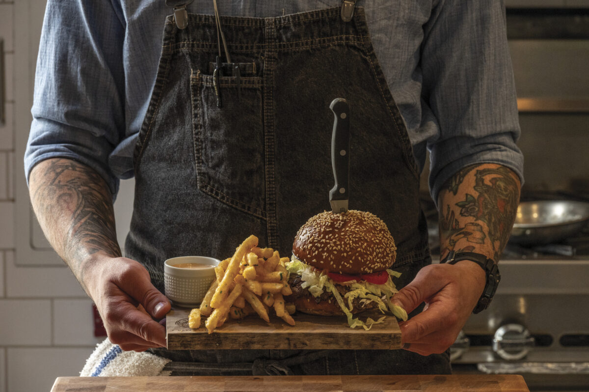 man with apron holding plate with burger and fries