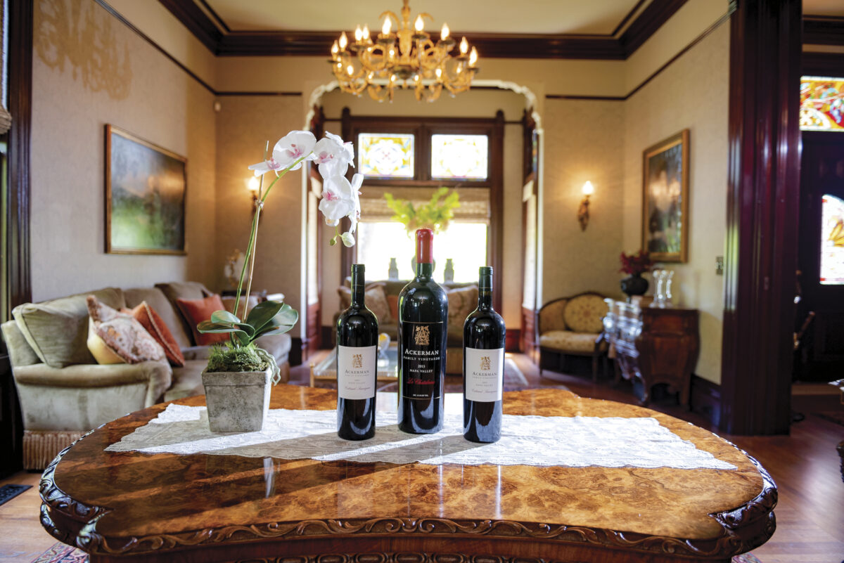 Interior image of the Ackerman Family Vineyards' Heritage House with 3 bottles of wine placed on a table with an orchid and seating area in the background