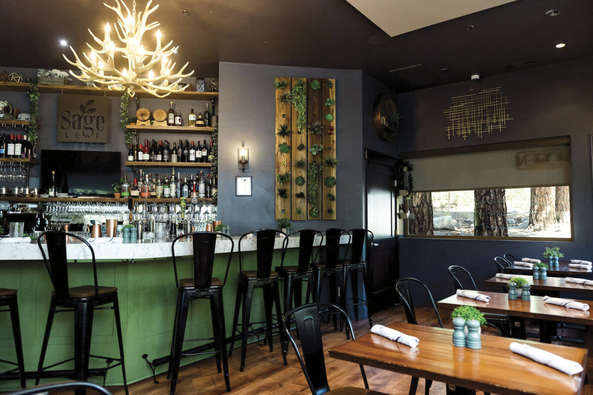 Interior of Sage Leaf Restaurant with wood floors, green bar with countertop and lit antler chandelier