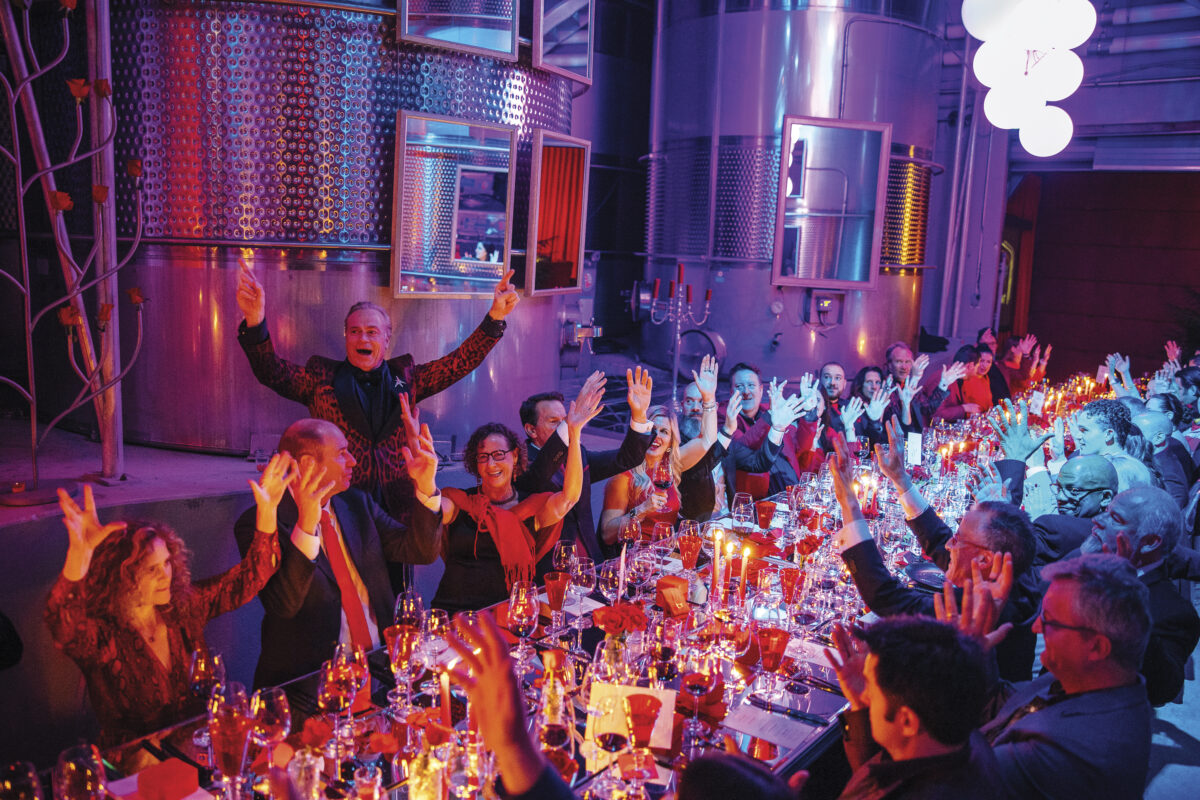 Jean-Charles Boisset standing behind large table of seated people, with arms up in celebration