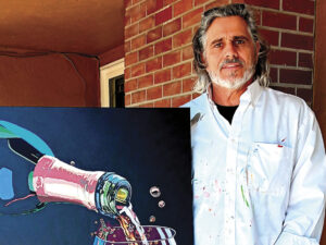 artist Chris Cammarata standing outside of a red brick building by one of his painting, a bottle of rose being poured into a glass