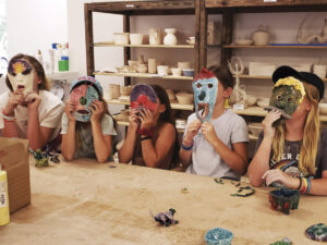 kids at table in pottery studio holding masks over their faces