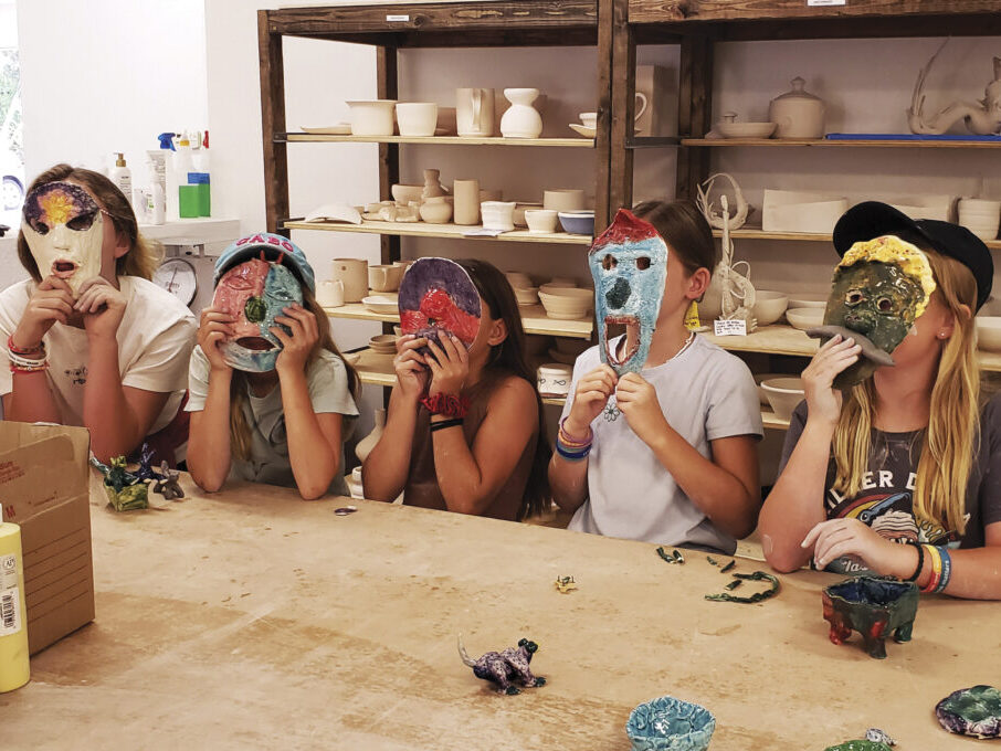 kids at table in pottery studio holding masks over their faces