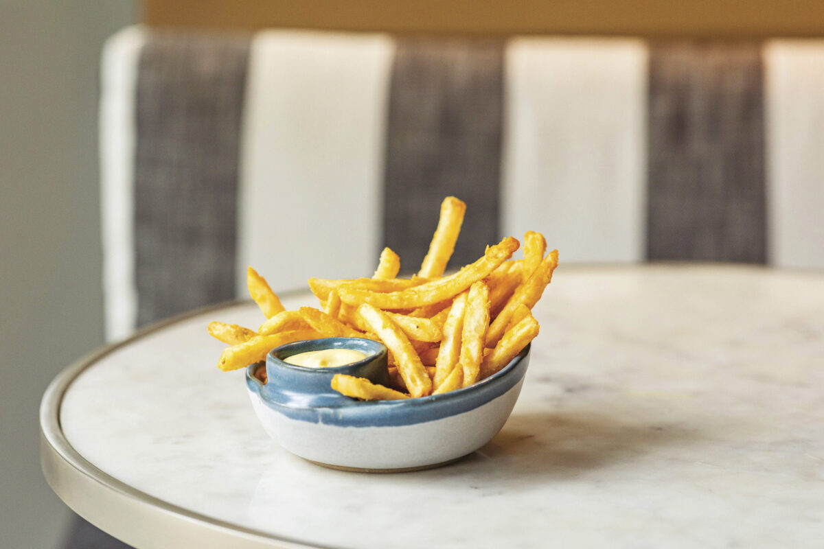 fries in white and blue pottery bowl on white table with gray and white stripe seat in the background