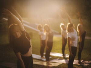 several women outside on yoga mats standing doing yoga with hazy sunny background