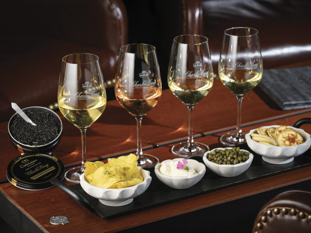 flight of wine with 4 glasses with a tin of Charles Krug branded caviar and additional food presented on wooden table