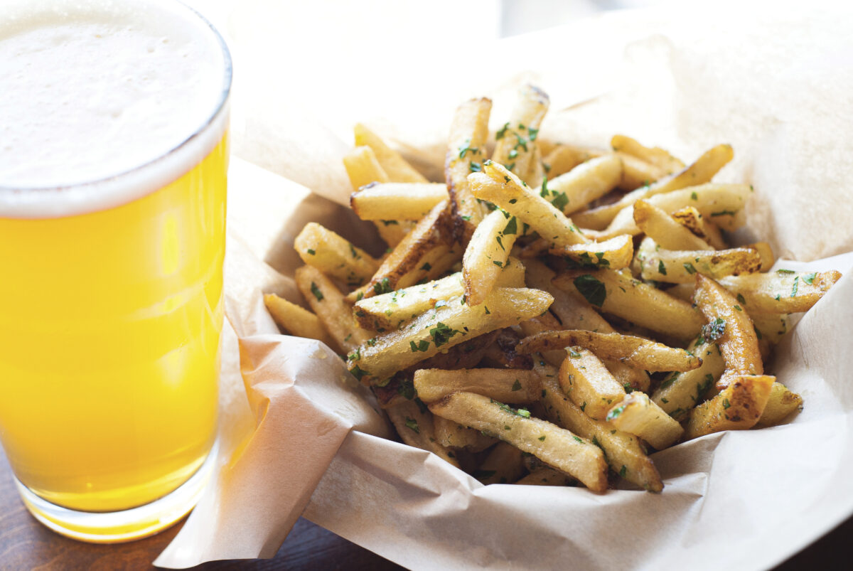 basket of french fries on paper with light pint of beer next to it