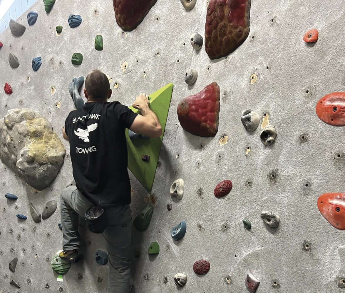 man indoor rockclimbing in black shirt and jeans