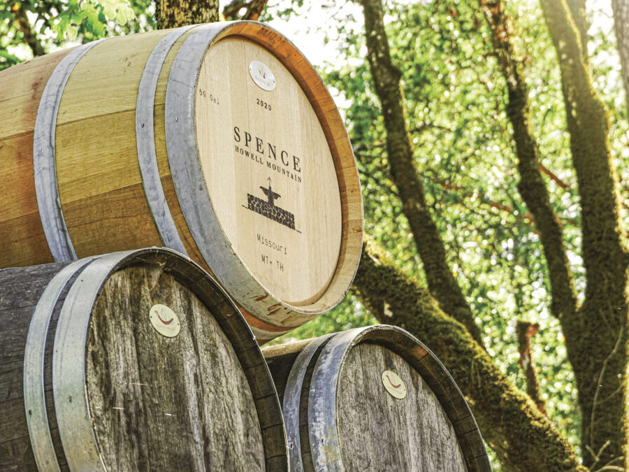 stack of wine barrels outside with Spence Vineyards logo on them with trees in the background