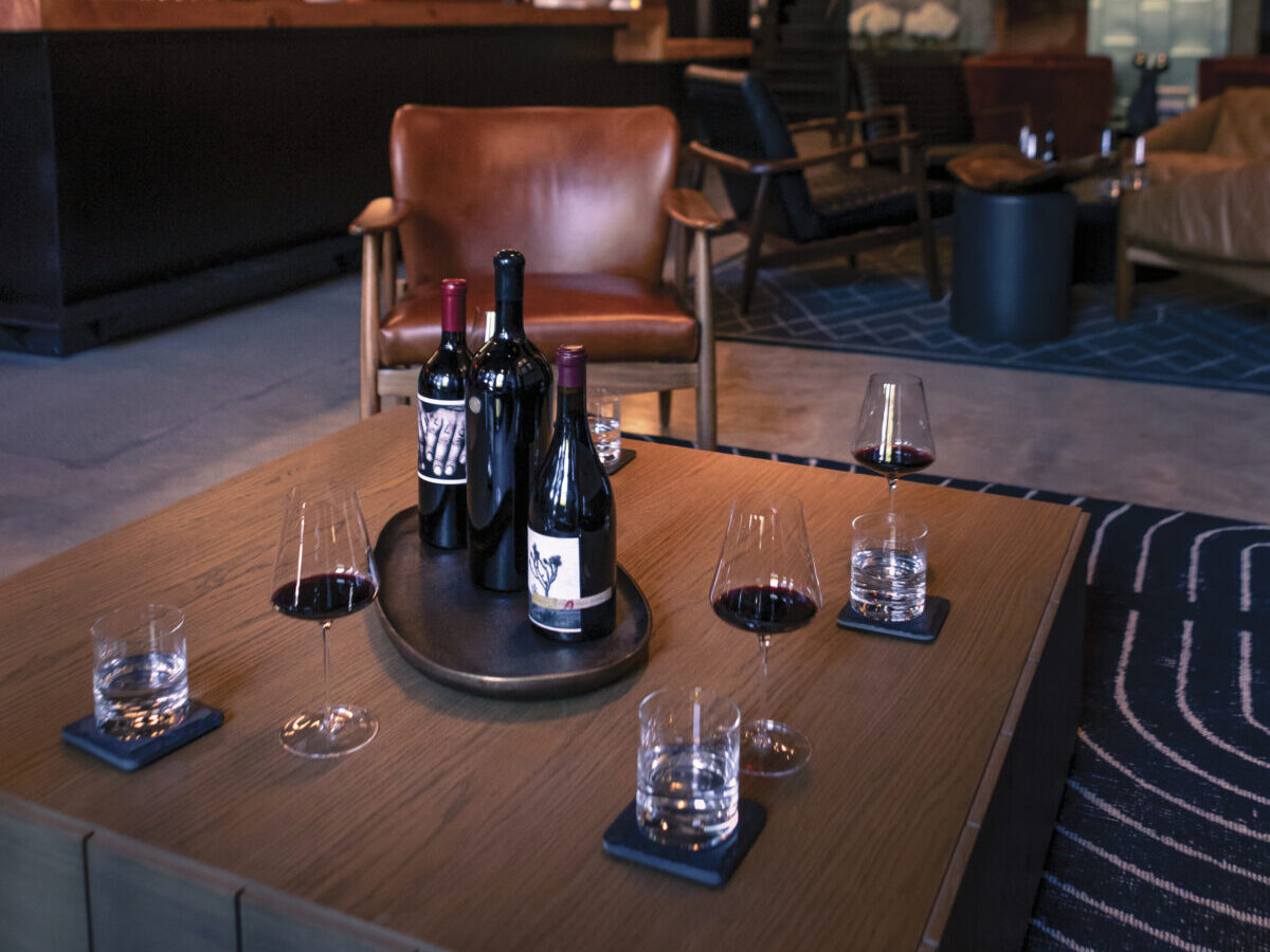 interior dimly-lit, moody room with leather chair ear wooden table with 3 glasses of water, red wine and a tray with 3 bottles of wine in the center