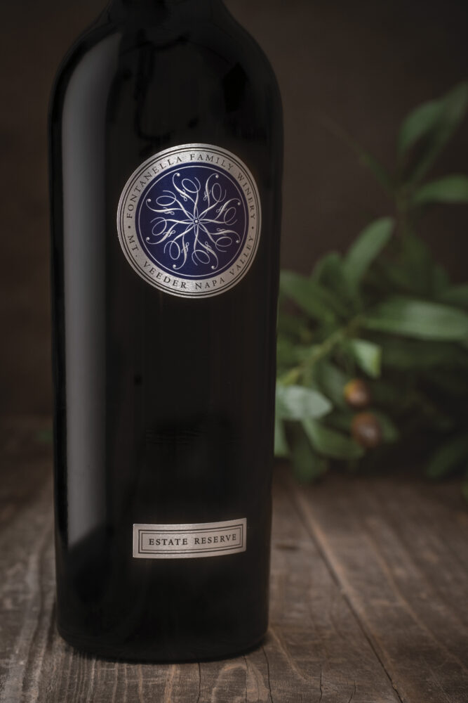 partial view of bottle of Fontanella Estate Reserve Cabernet on wood table with green plant in background