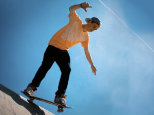 teenage boy in orange t-shirt and baseball cap backwards, skateboarding on a ramp