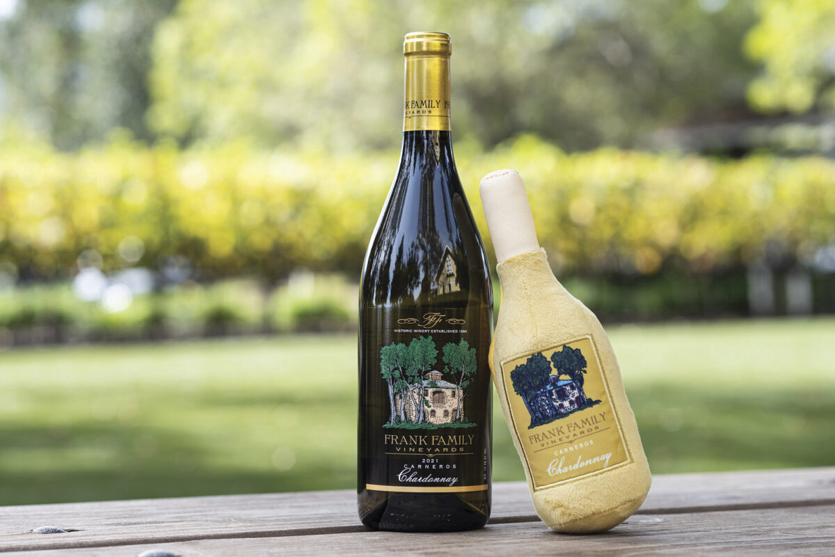 bottle of Frank Family wine on wood table with a stuffed dog toy version of the same bottle of wine