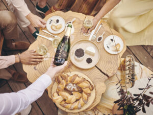 overhead view of table showing people seated at wooden table with plates of food and someone pouring wine