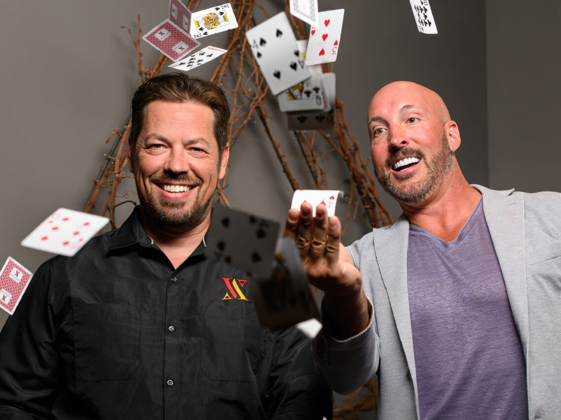 Mark Pickens, General Manager Ace & Vine in black shirt, with Mike LeBlanc, owner of The Lincoln + Ace & Vine in purple shirt and gray suit, both smiling with a deck of cards in the air