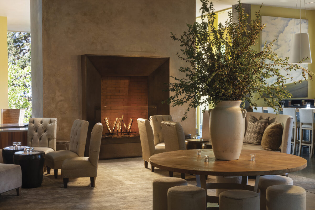 interior of hotel healdsburg with fire burning, large vase with greenery on table and several chairs around tables