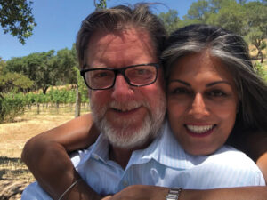 Sonya Franklin with arms around Al Franklin in front of a vineyard, smiling