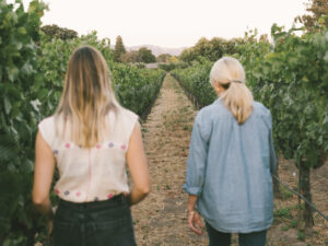 Hannah Gropman and Anne-Moller Racke walkin in vineyard away from camera in denim shirt and jeans