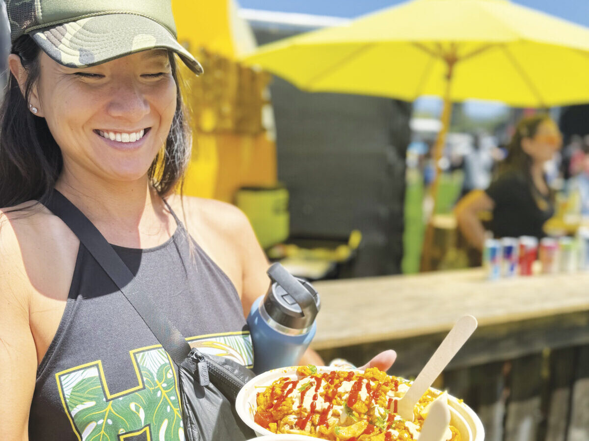 woman wearing hat at festival holding food and smiling