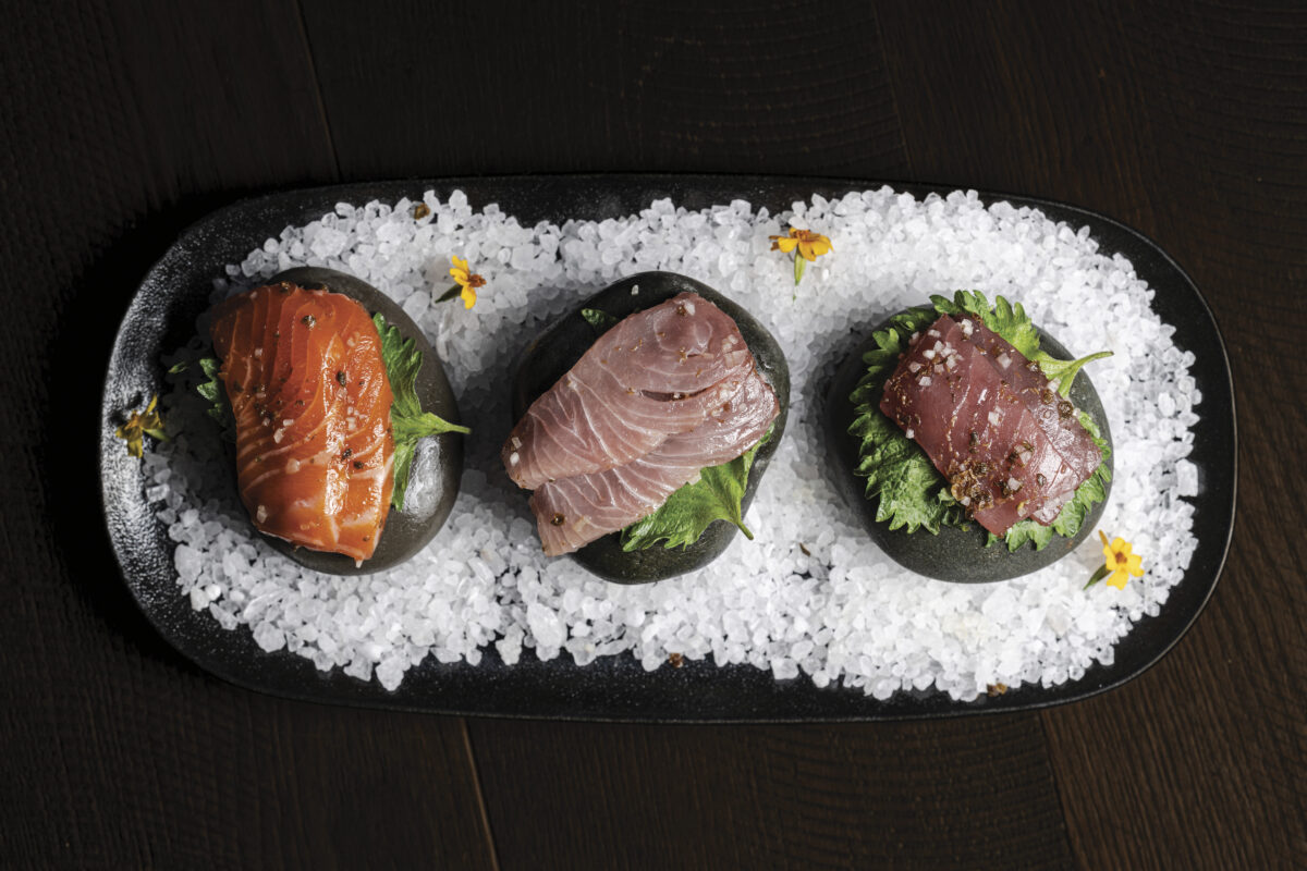 plate of food with 3 pieces of meat on three stones with white rock salt on dark oval plate on wood table